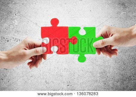 Partnership concept with hands putting green and red puzzle pieces together on concrete backgroud