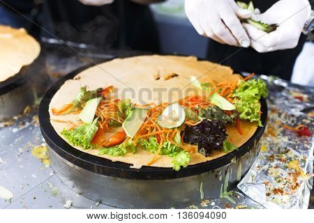 Making vegetable crepe at pan. Salty crepe or pancake with fillings made by street vendor's hands at outdoors creperie. French cuisine, cooking for commercial kitchen.