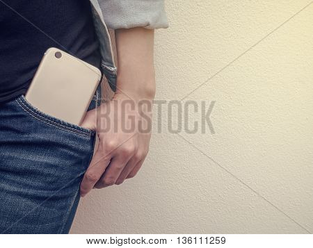 Close up of mobile phone in jeans pocket with poses hand of a person standing against the wall with copy space and Vintage filter