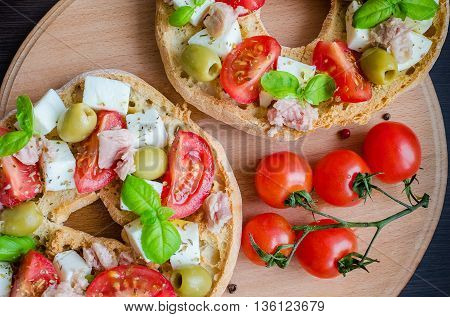 Classical frisella tomato cheese mozzarella tuna and olives. Italian starter friselle. Dried bread called freselle on wooden board with tomatoes cherry. Italian food. Healthy vegetarian food.