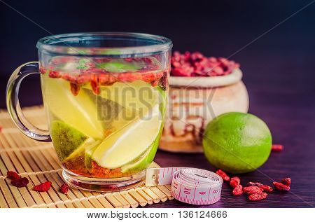 Cup of delicious dietary Goji berry tea with lime on wooden background with measuring tape. Wolfberry for a healthy diet. Alternative medicine. Recovery. Rejuvenation. Slimming. Selective Focus.