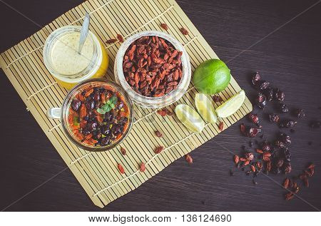 Fresh antioxidant herbal tea from dried goji berries sweetbrier and blueberry in a glass cup on wooden background with lime and honey. Healthy food. Alternative medicine. Top view.Mystic light style.