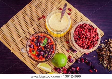 Still life glass cup of herbal tea with lime honey goji berries sweetbrier and blueberry on wooden background. Healthy food. Alternative medicine. Selective focus. Top view.