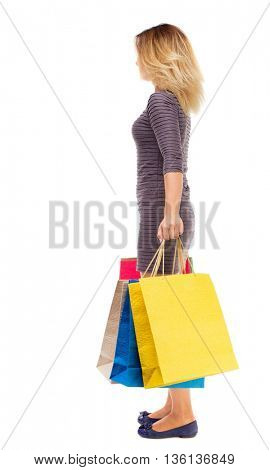 back view of woman with shopping bags . beautiful brunette girl in motion.  backside view of person. Girl in purple dress is standing sideways and holding shopping bags.