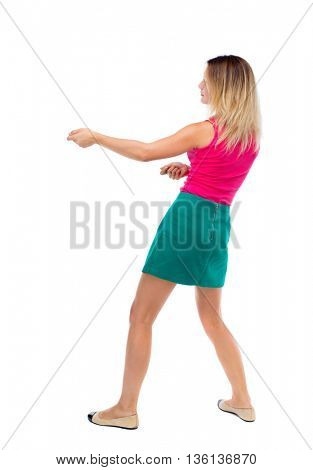 back view of standing girl pulling a rope from the top or cling to something. girl  watching. backside view of person. blonde in a green skirt and pink sweater leaning legs pulls the rope.