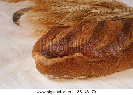 bunch of mown wheat ears with vintage handmade reaper hook sickle and rye dark white french fresh bread loaf on light linen tablecloth