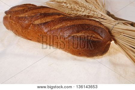 bunch of mown wheat ears with vintage handmade reaper hook sickle and rye dark white french fresh bread loaf on light linen tablecloth