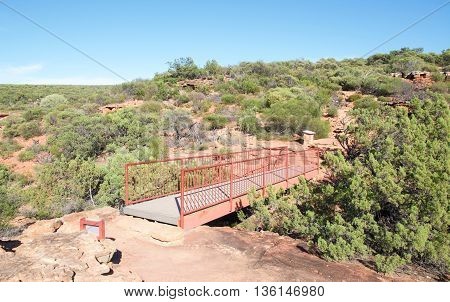Z-bend bridge between the sandstone rock bluffs with native flora in the Z-bend landscape under a clear blue sky in Kalbarri National Park in Western Australia.