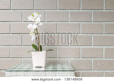 Closeup artificial plant with white orchid flower on pink flower pot on wood weave table on blurred brown brick wall texture background beautiful interior in relaxation concept of house