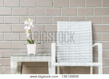 Closeup artificial plant with white orchid flower on pink flower pot on wood weave table with wood weave chair on blurred brown brick wall texture background beautiful interior in relaxation concept