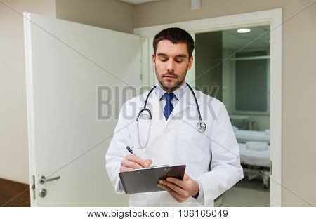 medicine, healthcare and people concept - doctor writing to clipboard at hospital
