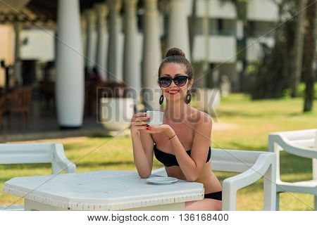 Sexy woman in bikini in Asia at beach cafe bar.Girl enjoying a cup of coffee outside. Smiling happy Caucasian woman near ocean beach. young beautiful woman relaxing on tropical vacation in Asia