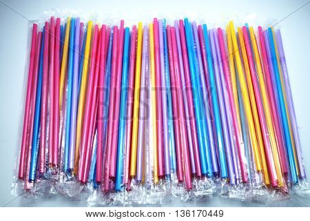 Colorful plastic drinking straws in plastic wraps on blue-white background. Focus on extended straws. Space for texts.