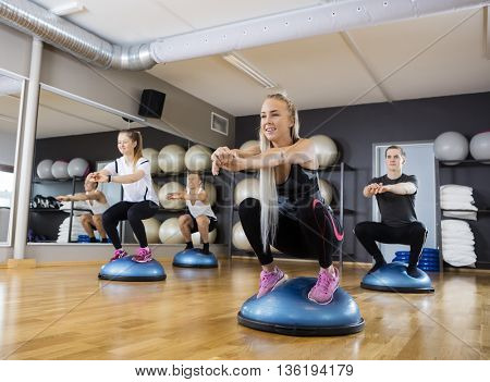 Friends Doing Squatting Exercise On Bosu Ball In Gymnasium