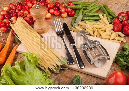 Italian food background, with vine tomatoes, basil, spaghetti, mushrooms, olives, parmesan, olive oil, garlic, peppercorns, rosemary, parsley and thyme. Slate background.