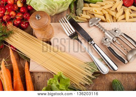 Italian food background, with vine tomatoes, basil, spaghetti, mushrooms, olives, parmesan, olive oil, garlic, peppercorns, rosemary, parsley and thyme. Slate background.