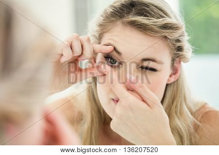 Young woman applying contact lens while looking in mirror