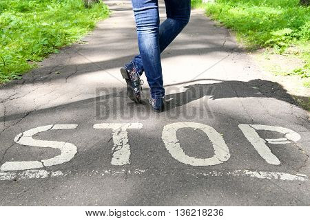 Stop sign painted on the road and female legs next to the sign.