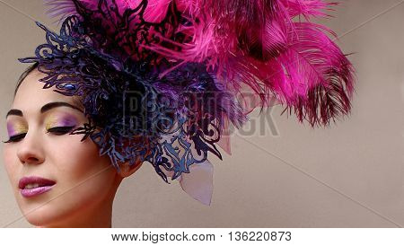 Close-up portrait of beautiful young woman in lace lilac purple hat fascinator with feathers on grey background. Fashion professional violet purple shades make-up. Model shot.
