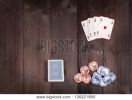 Chips and Four aces vintage poker game playing cards on a weathered wood table view from above.