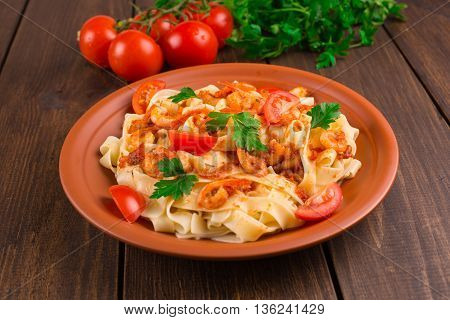 Fettuccine pasta with shrimp tomatoes and herbs. wooden background