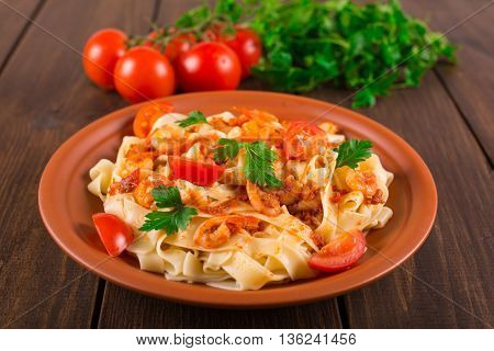 Fettuccine pasta with shrimp tomatoes and herbs. wooden background
