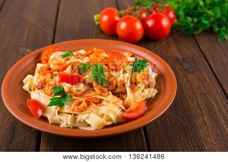 Fettuccine pasta with shrimp tomatoes and herbs. wooden background