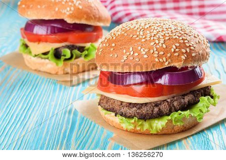 Two homemade cheeseburgers with beef patties and fresh salad on seasame buns, sered on blue wooden table.