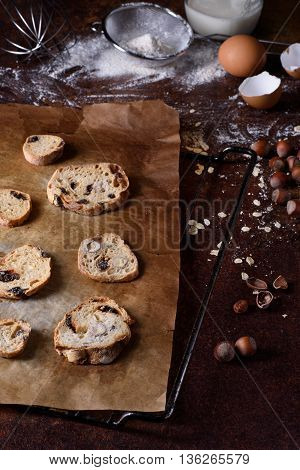 Baked bread rusks with raisins and nuts, cooking ingredients over rustic kitchen table. Brussels hazelnut biscuits, crispy appetizers.
