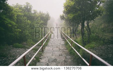 lonely in the rain a woman in black cloths with cover red umbrella walking down the stone stairs in the rain and fog.