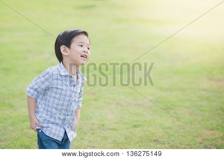 Cute Asian chid running on green grass under sunlight