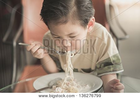 Cute Asian chid eating Spaghetti Carbonara in restaurant vintage fiter