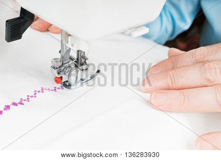 Seamstress using sewing machine close-up. Woman hand sewn white cloth