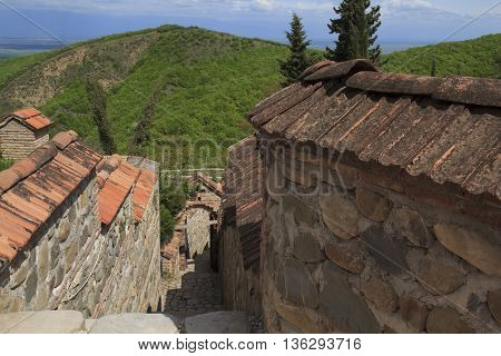 ancient stony bystreet downhill with orange tiles and green mountain view in Georgia