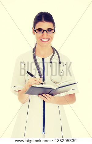 Young female doctor wirting in a book.
