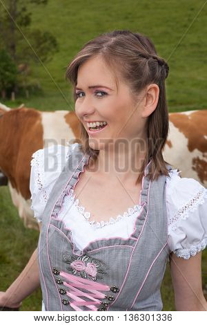 Portrait of a young peasant woman in dirndl that looks laughing at the camera.
