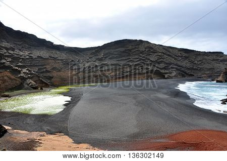 black lava sand beach with green water at El Gordo on spanish volcanic island Lanzarote