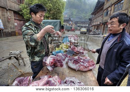 Zhaoxing Dong Village Guizhou Province China - April 8 2010: A street vendor weighs pork on Chinese scales.