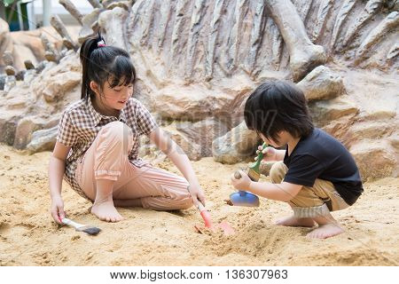 Little asian children has fun digging in the sand at adventure park