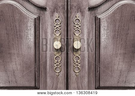 Stylish brass door handles on a hardwood cabinet or closet with ornate escutcheons and raised panels on the doors in a close up frontal view conceptual of furnishing and interior decor