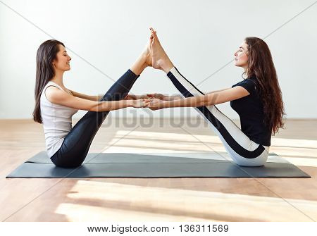 Two Young Women Doing Yoga Asana Buddy Boat Pose
