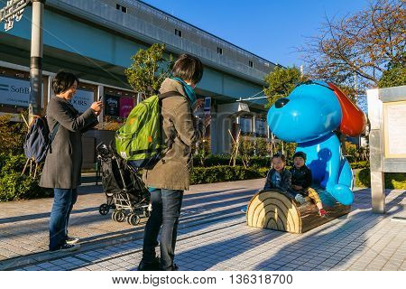 TOKYO JAPAN - NOVEMBER 27 2015: Unidentified Japanese families with a cartoon dog statue in front of Fuji Television Headquaters building in Odaiba area