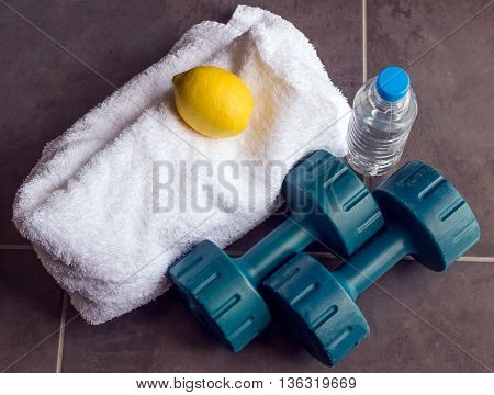Concept - sports. Dumbbells are next to a white towel bottle of water and lemon.