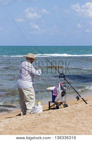 Acre Israel - May 28 2016: Elderly man fishing with a fishing rod on the beach in Akre Israel