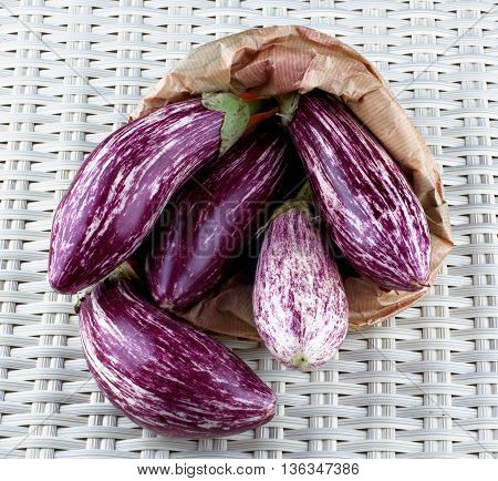 Heap of Fresh Raw Striped Eggplants into Paper Bag closeup on Wicker background