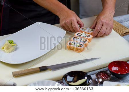 Man's hands touch sushi rolls. White plate on cooking board. Uramaki rolls prepared by cook. Favorite dish of gourmets.