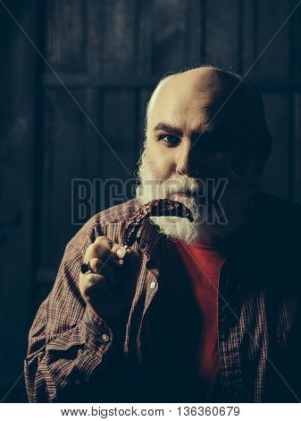 Old bearded man with long grey beard on smiling face in checkered shirt with red chilli pepper or capsicum on wooden wall background