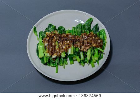 Kale fried in oyster sauce on white dish and background blue.