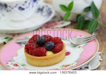 Delicious crunchy tartelette with custard, fresh raspberries and blueberries on pink plate