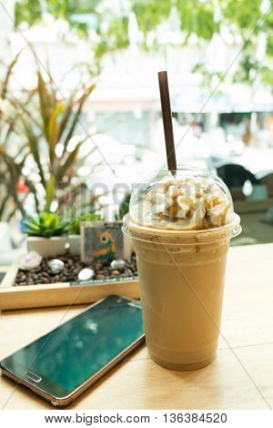 Latte frappe topping with whipping cream in takeaway cup and mobile phone on table in coffee shop.